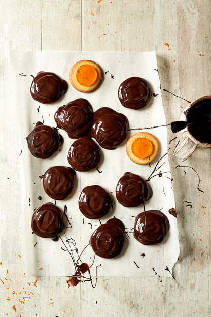 Flat lay of handmade chocolate jaffa cakes styled on a vinyl photography backdrop featuring a faded light wood effect with vertical wood grain patterns.