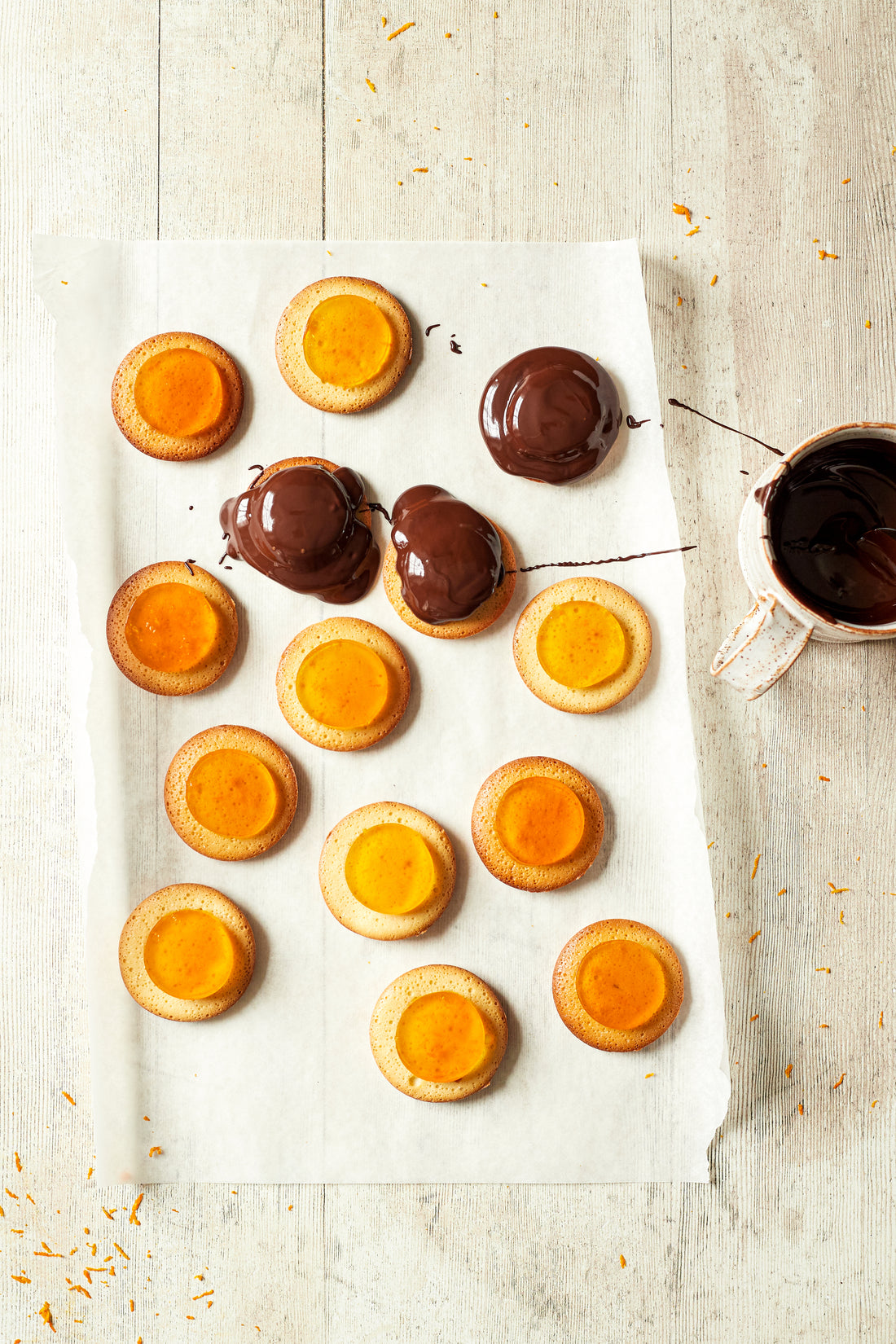 Flat lay of handmade jaffa cakes styled on a vinyl photography backdrop featuring a faded light wood effect with vertical wood grain patterns.