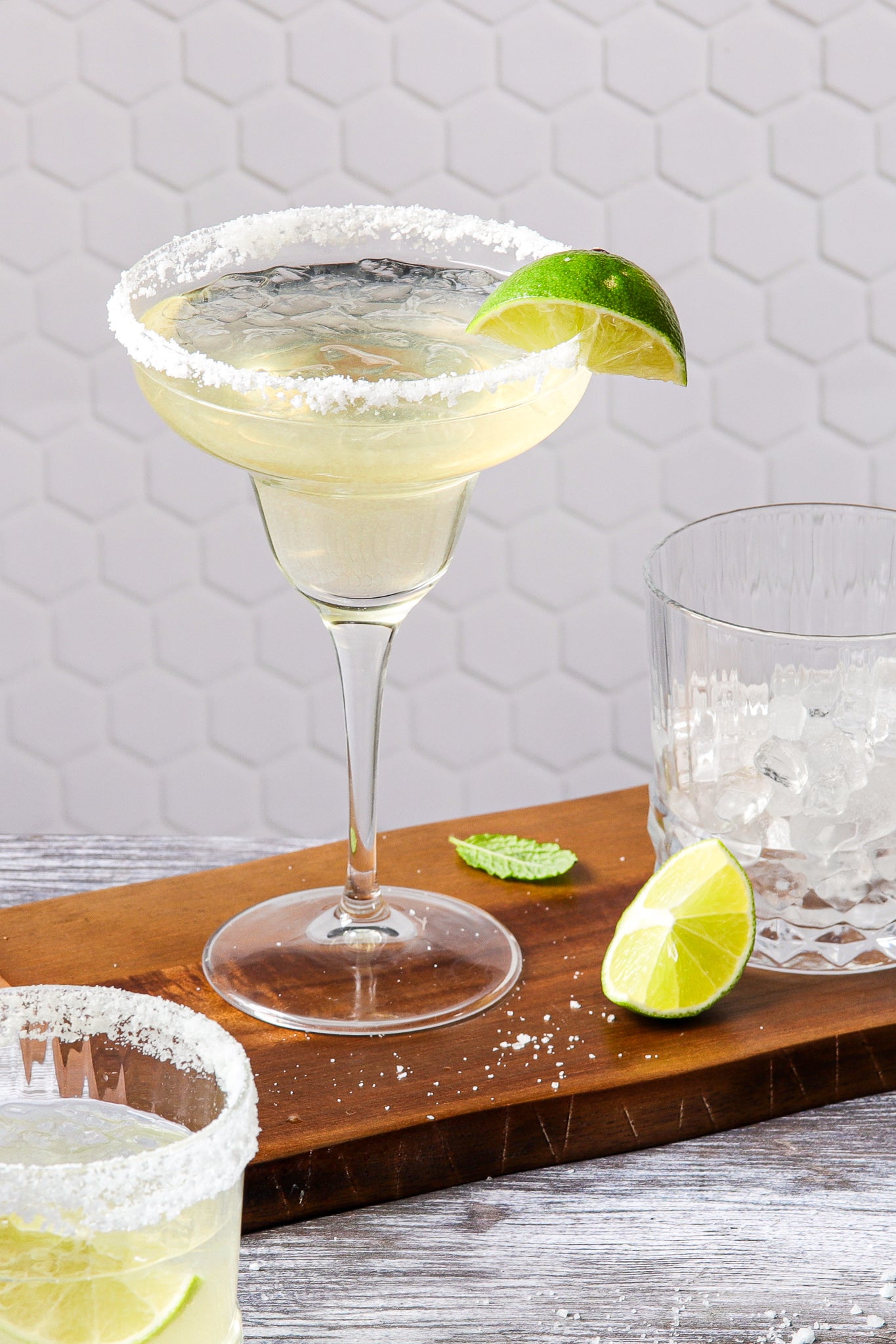 Classic margarita cocktail styled against a white hexagonal tile-effect photography backdrop.