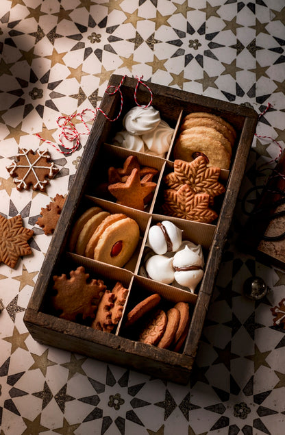 A white vinyl photography backdrop with a neutral beige and faded blue-grey star pattern, with a wooden box of Christmas biscuits on top.